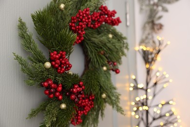Beautiful Christmas wreath with red berries and decor hanging on white door, closeup. Space for text