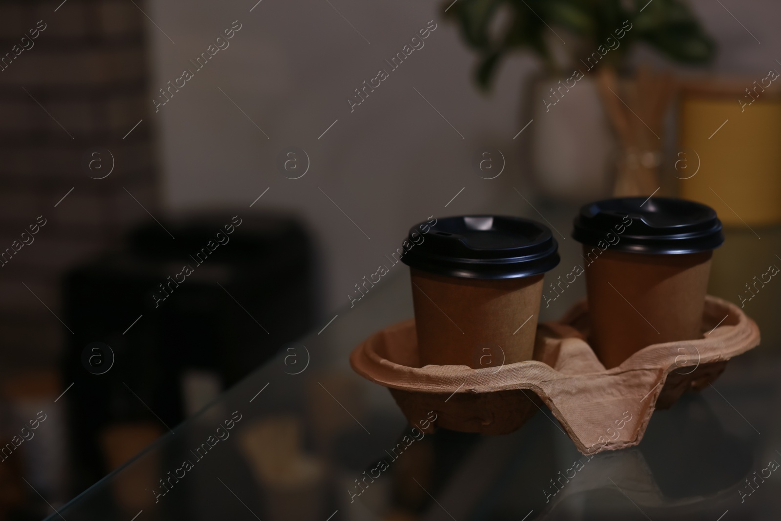 Photo of Takeaway coffee cups with cardboard holder on glass table in cafe. Space for text