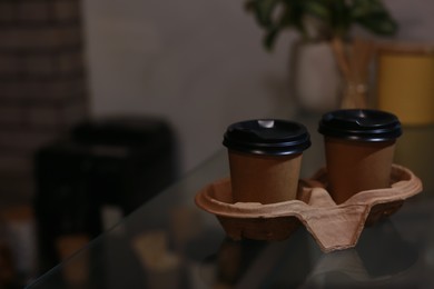 Photo of Takeaway coffee cups with cardboard holder on glass table in cafe. Space for text