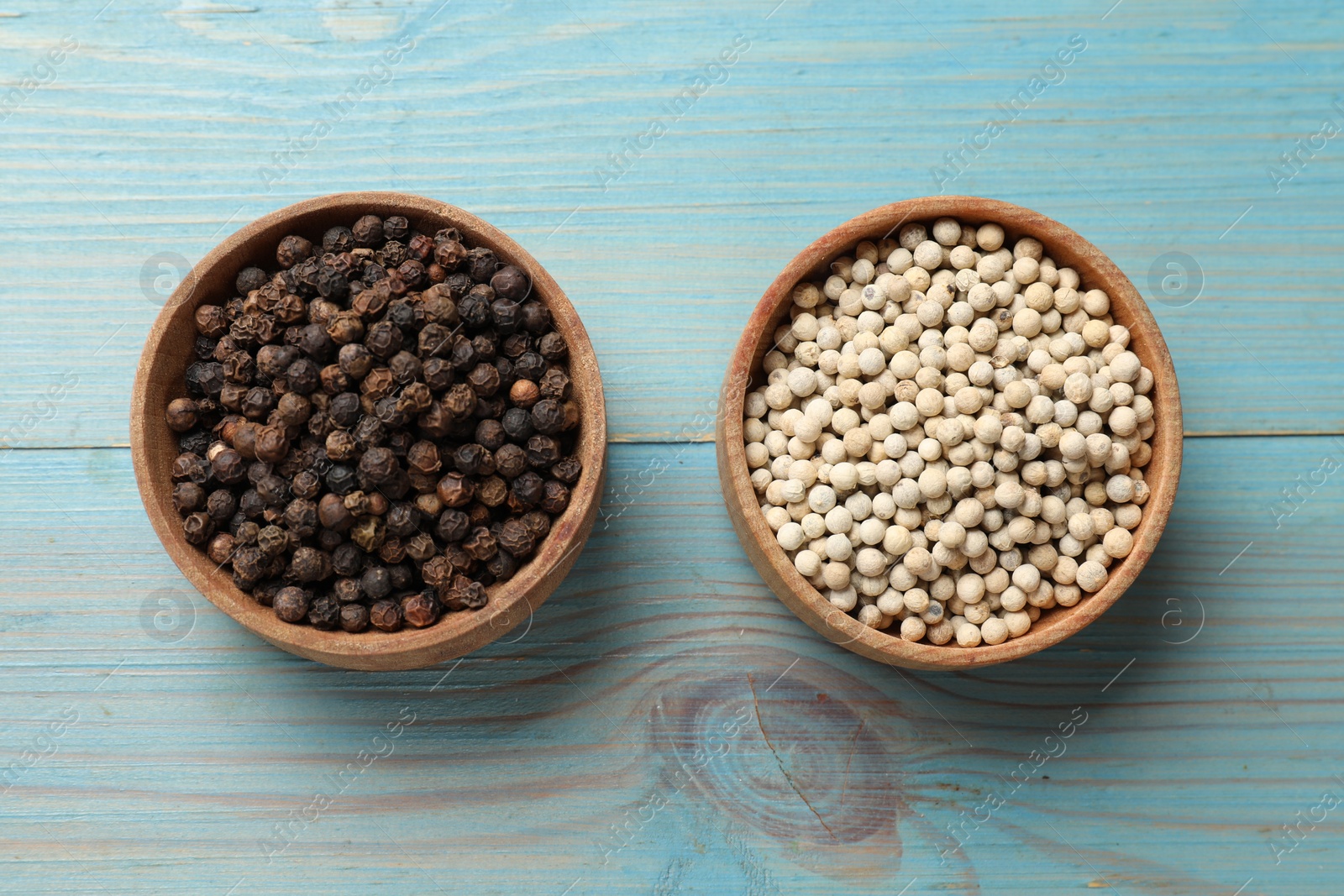 Photo of Aromatic spice. White and black peppers in bowls on light blue wooden table, top view