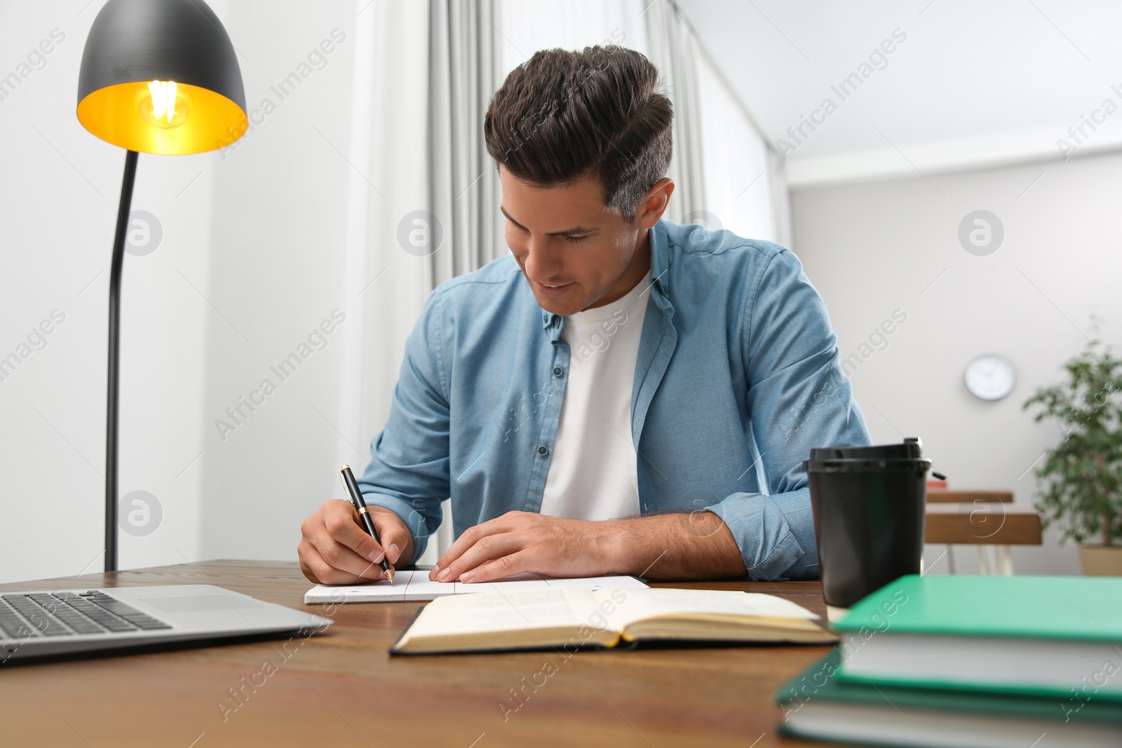 Photo of Man with laptop and book studying at table in library