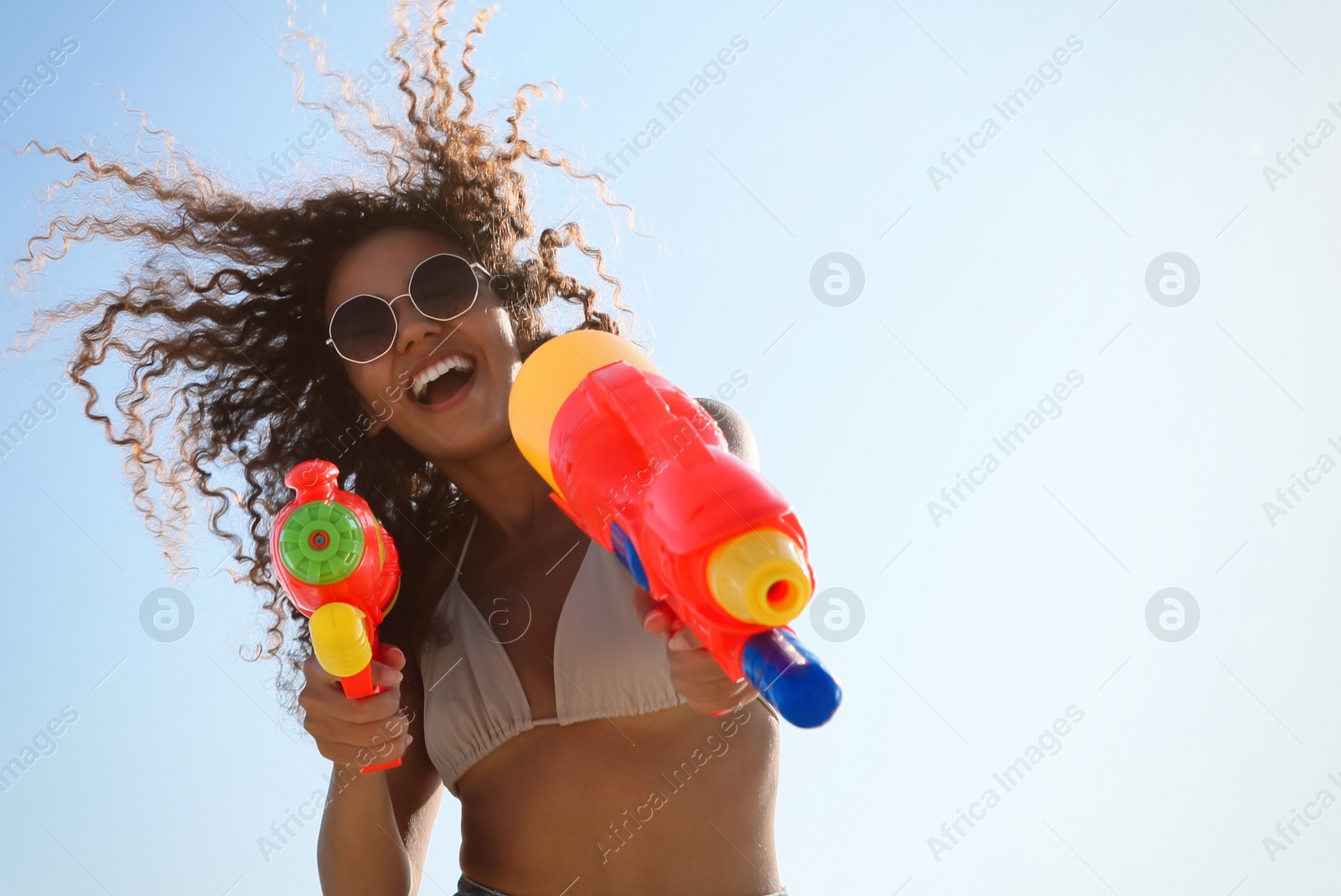 Photo of African American woman with water guns against blue sky, low angle view. Space for text
