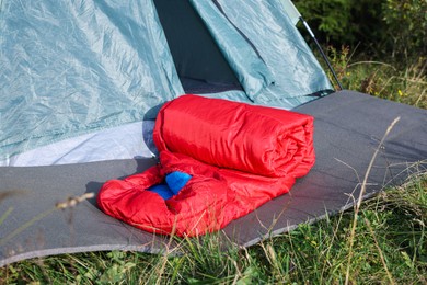 Photo of Red sleeping bag near camping tent on green grass outdoors