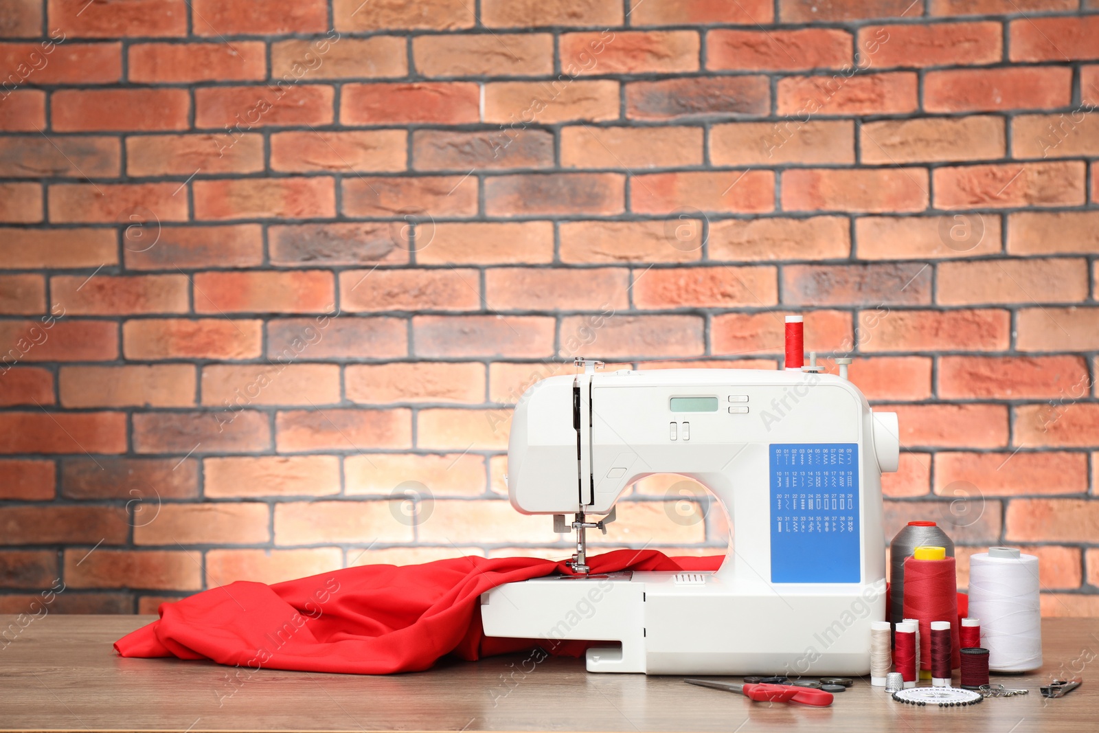 Photo of Sewing machine with fabric and craft accessories on wooden table against brick wall