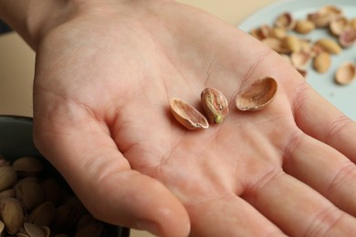 Photo of Woman holding tasty peeled pistachio nut at table, closeup