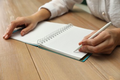 Photo of Left-handed woman writing in notebook at wooden table, closeup