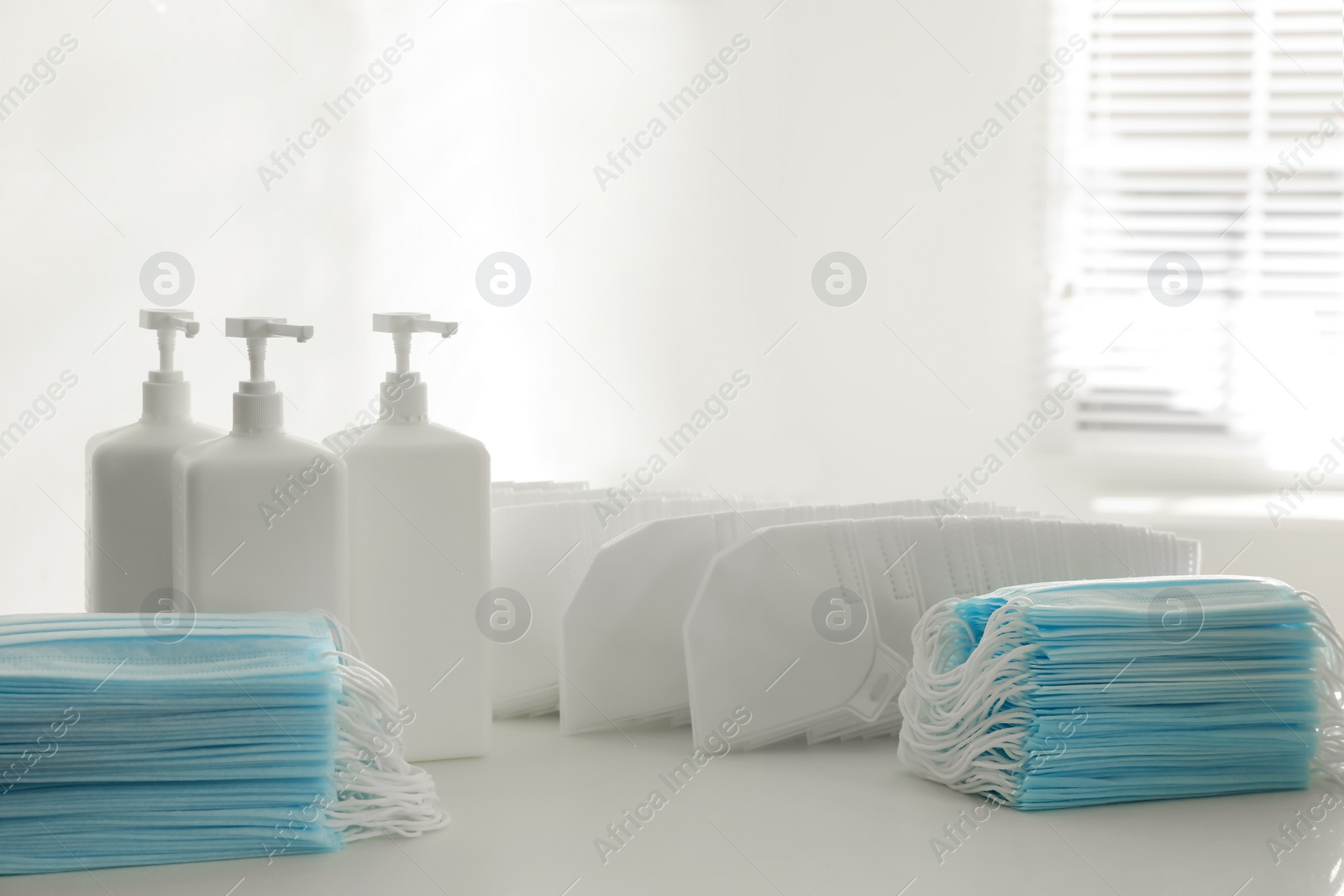 Photo of Hand sanitizers and respiratory masks on white table indoors. Protective essentials during COVID-19 pandemic