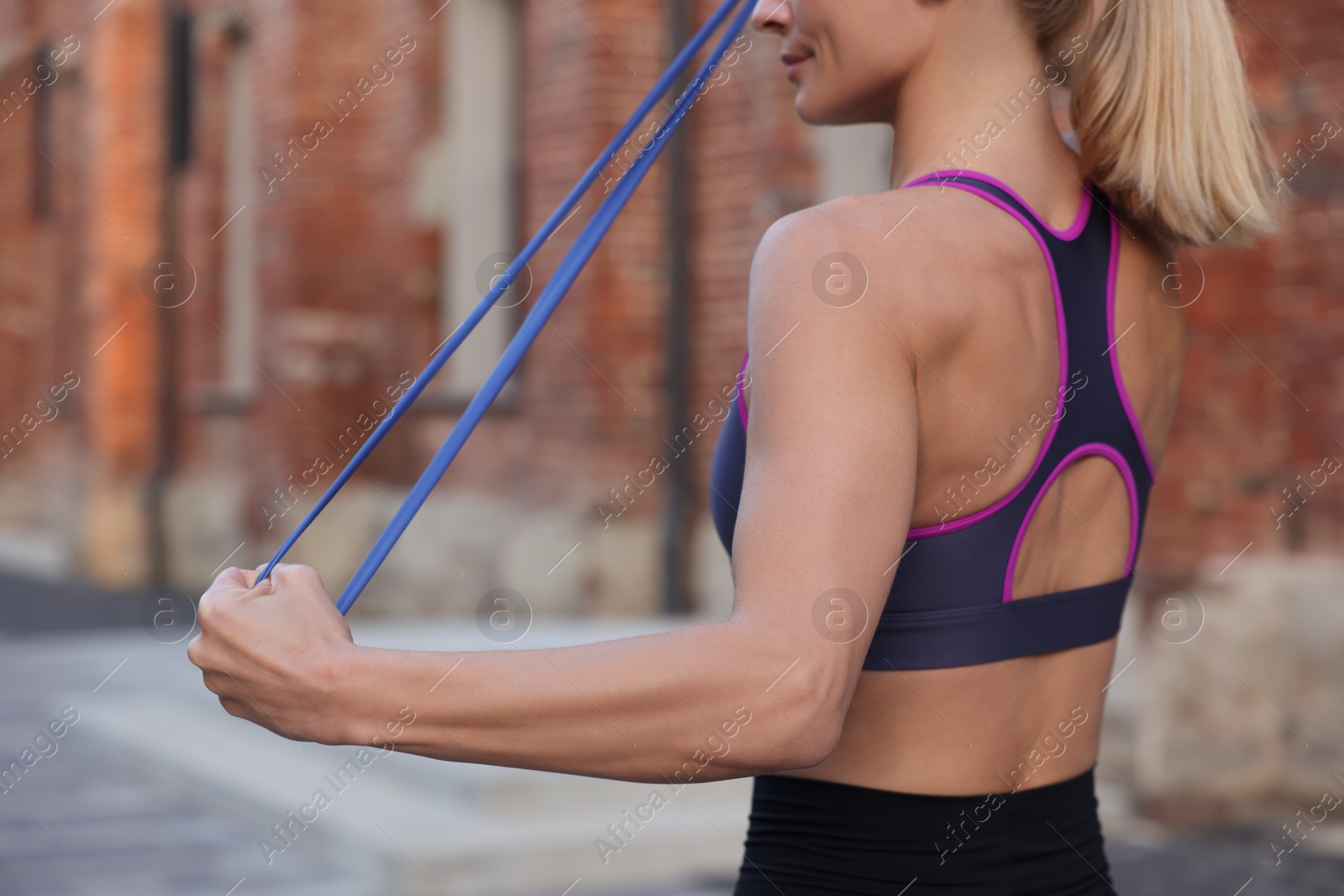 Photo of Woman doing exercise with fitness elastic band outdoors, closeup