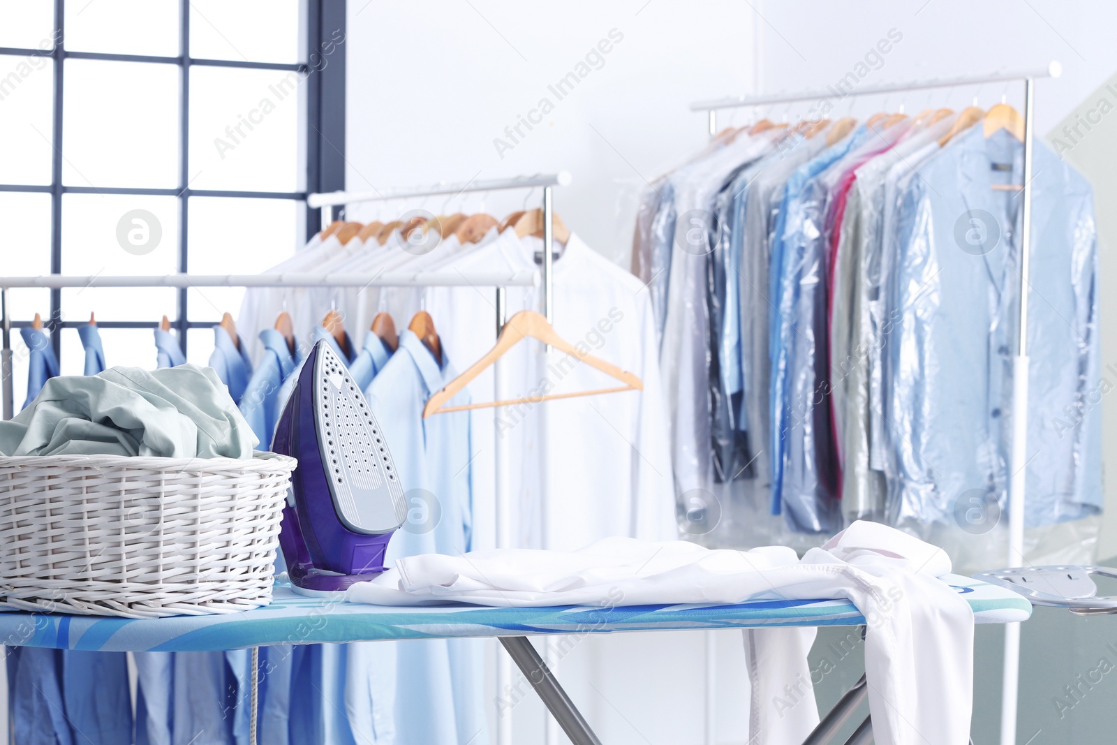 Photo of Wicker basket with clothes on ironing board at dry-cleaner's