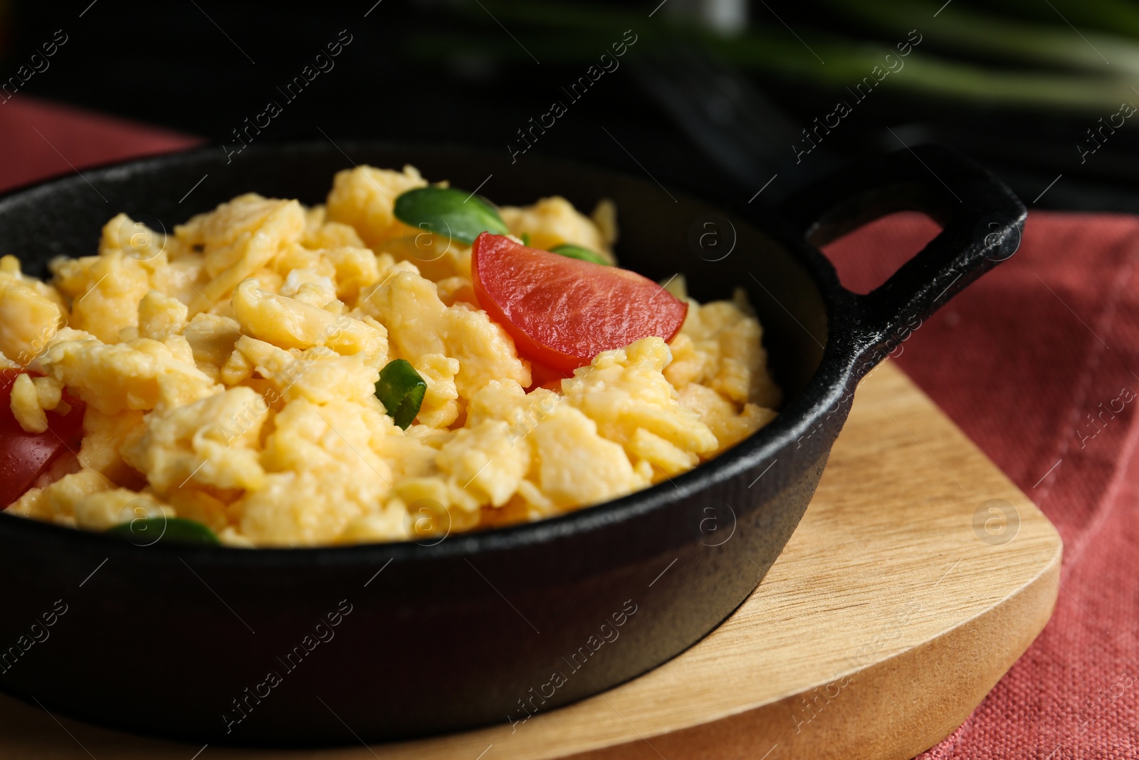 Photo of Tasty scrambled eggs with sprouts and cherry tomato in frying pan on table, closeup