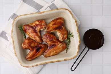 Photo of Fresh marinade, chicken wings and rosemary on white tiled table, top view