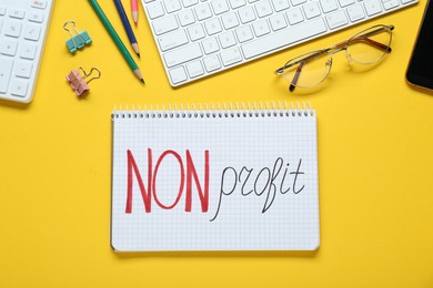 Photo of Non profit. Flat lay composition with notebook, glasses and stationery on yellow background