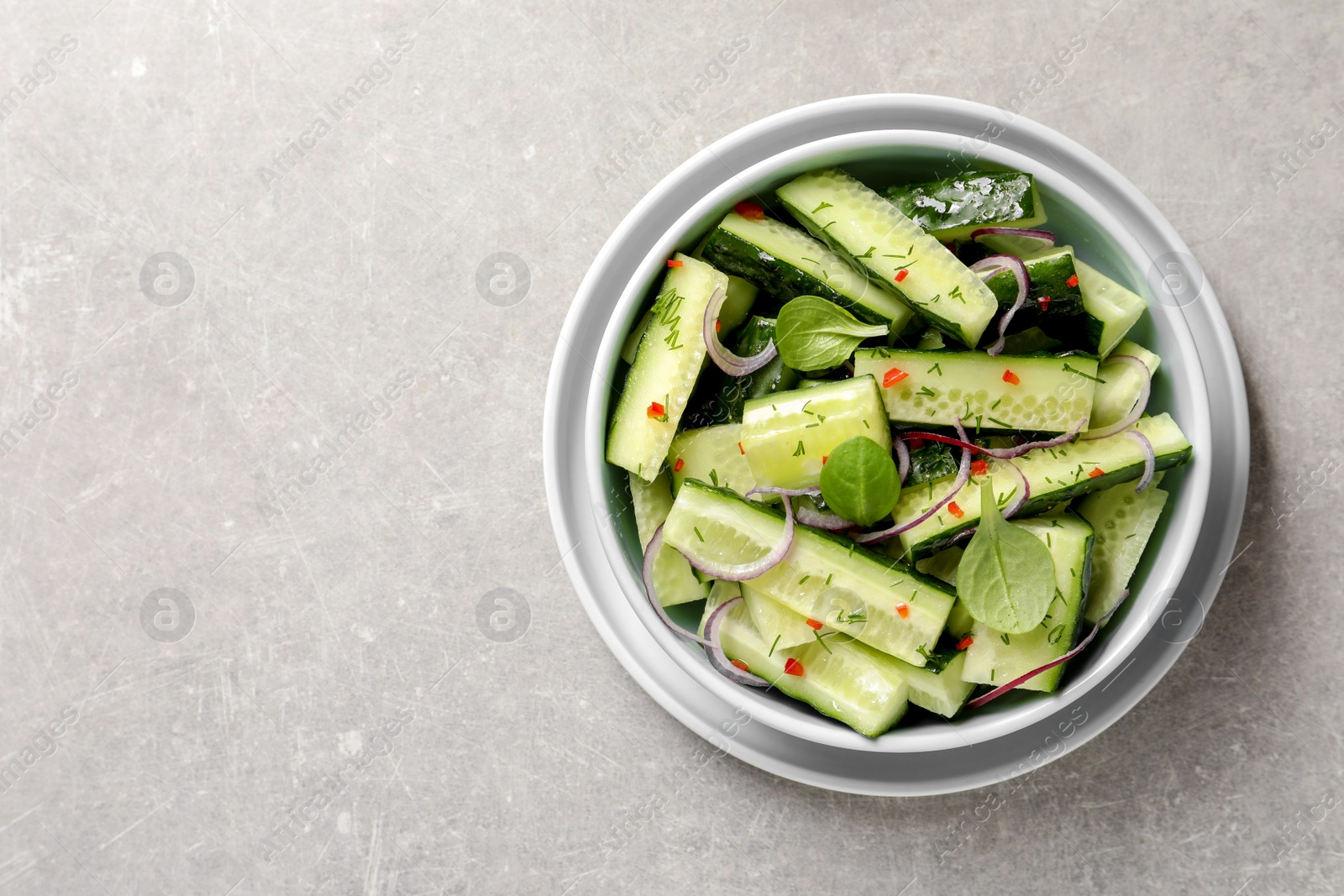 Photo of Delicious cucumber salad with onion and spinach in bowl on grey background, top view. Space for text