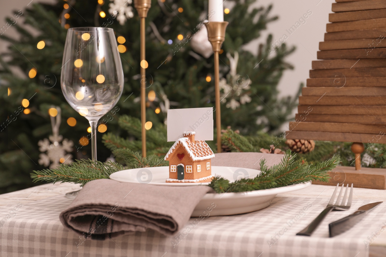 Photo of Festive place setting with beautiful dishware, cutlery and gingerbread house card holder for Christmas dinner on white wooden table