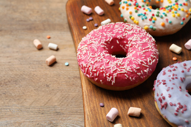 Photo of Yummy donuts with sprinkles and marshmallows on wooden table, closeup