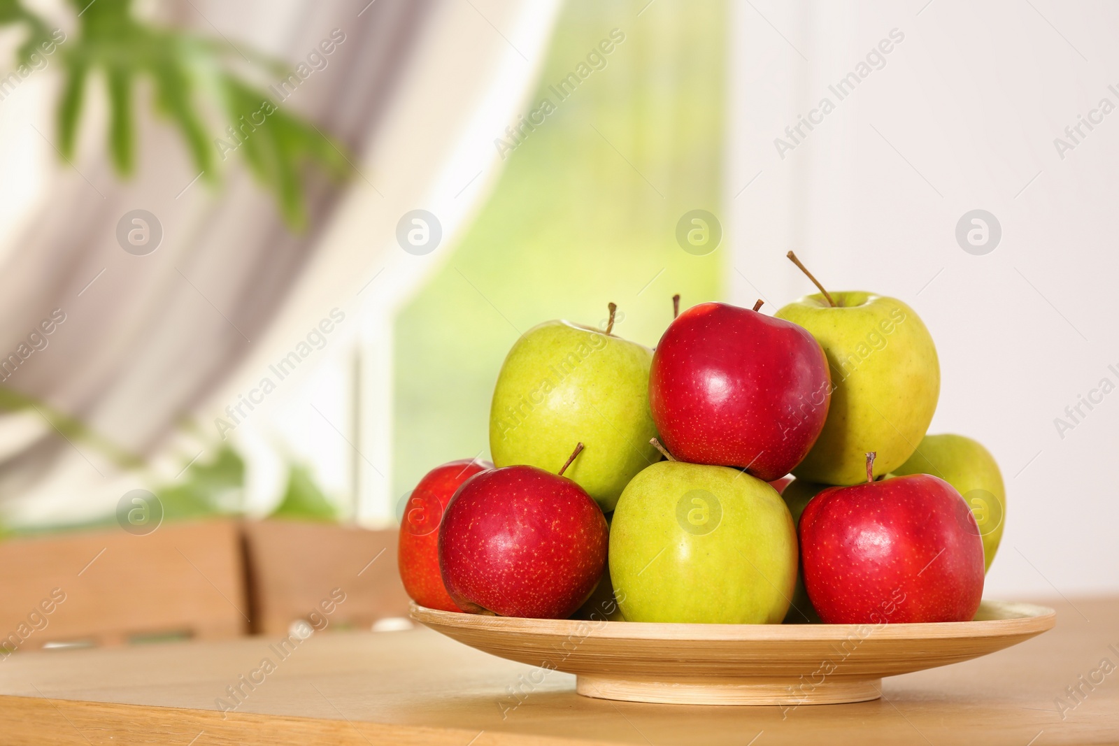 Photo of Plate with different sweet apples on table in room, space for text