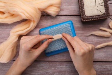 Photo of Woman felting from wool at wooden table, top view