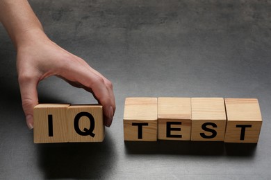 Woman taking cubes with text IQ Test on grey background, closeup