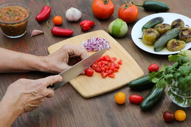 Photo of Woman cutting tomato for salsa sauce at wooden table, closeup