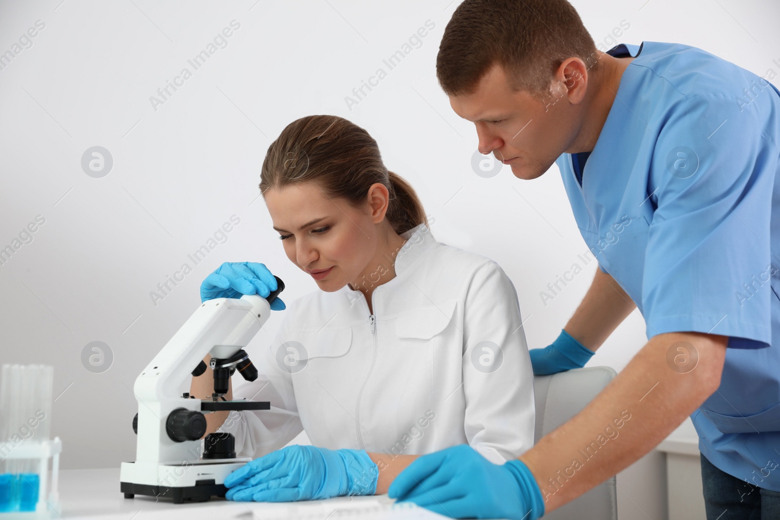 Photo of Scientist with microscope at table and colleague in laboratory. Medical research