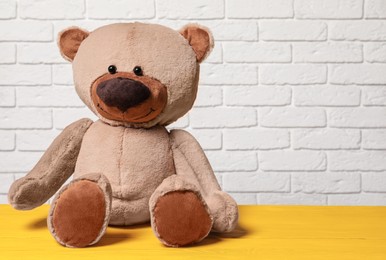Photo of Cute teddy bear on yellow wooden table near white brick wall, space for text