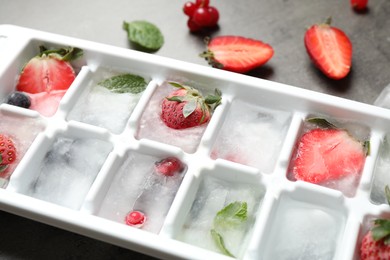 Photo of Ice cubes with berries in tray on grey table, closeup