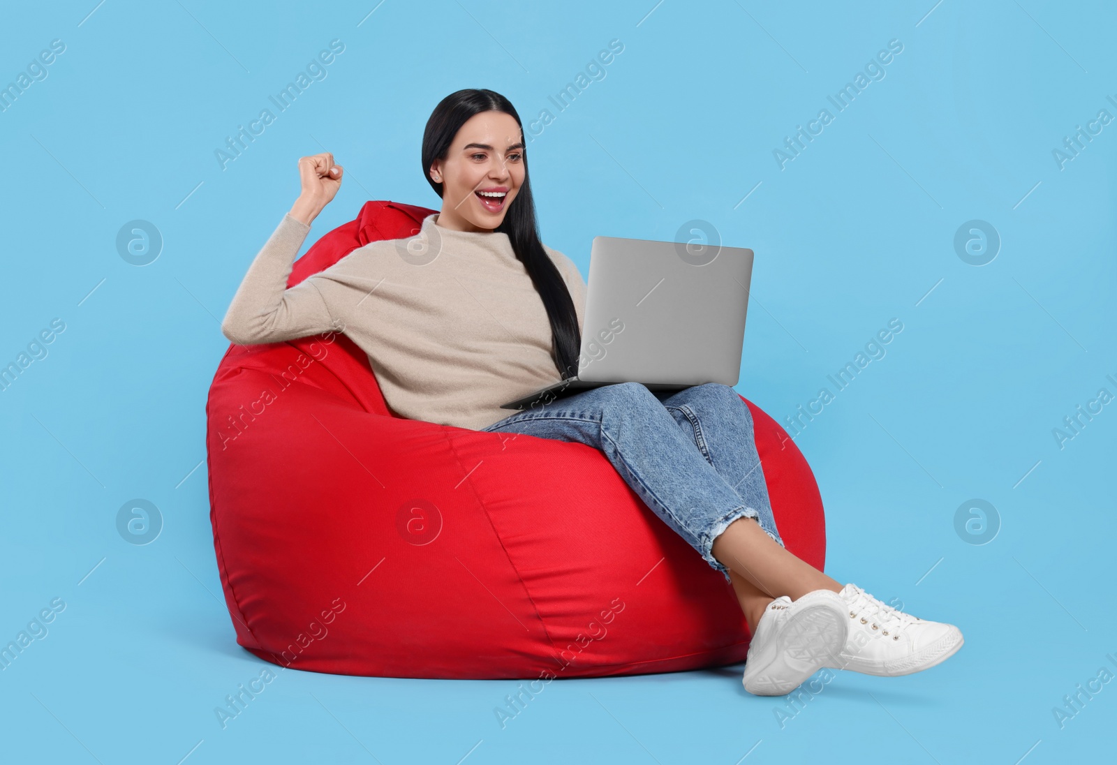 Photo of Cheerful woman with laptop sitting on beanbag chair against light blue background