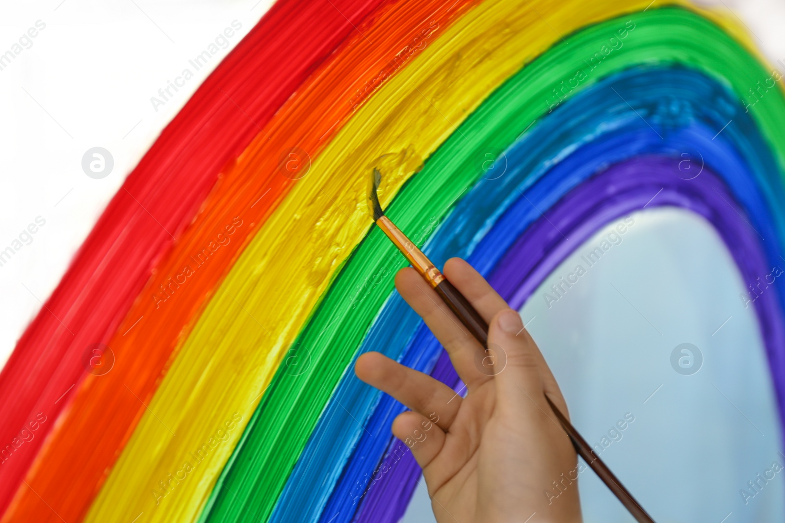 Photo of Little child drawing rainbow on window, closeup. Stay at home concept