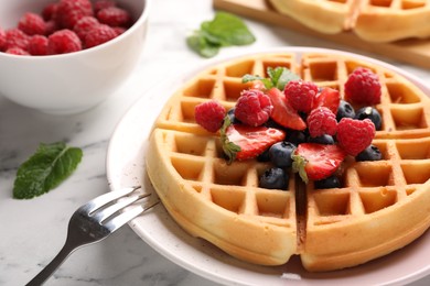 Photo of Tasty Belgian waffle with fresh berries and fork on white marble table, closeup