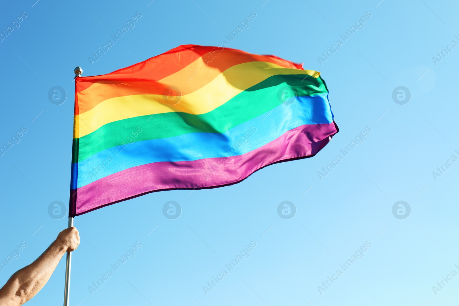 Photo of Gay man holding rainbow LGBT flag on blue sky background. Space for text