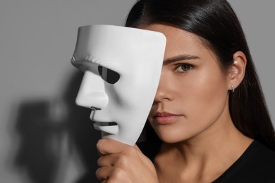 Multiple personality concept. Woman with mask on grey background