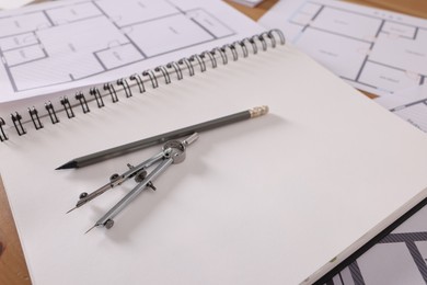 Photo of Sketchbook with construction drawings, pair of compasses and pencil on wooden table, closeup