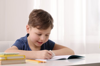 Little boy erasing mistake in his notebook at white desk indoors