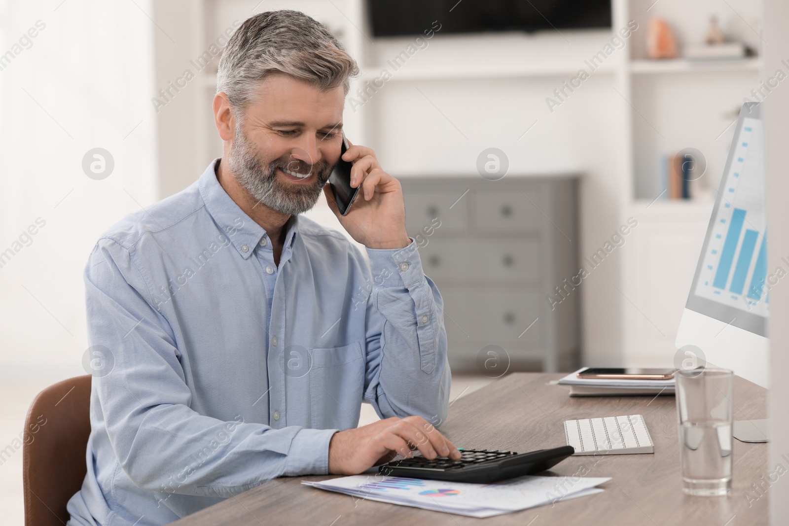 Photo of Professional accountant talking on phone and working at wooden desk in office