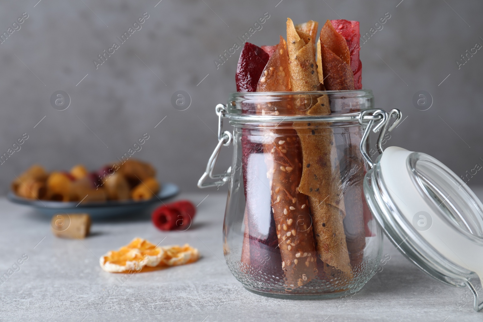 Photo of Delicious fruit leather rolls on grey table. Space for text