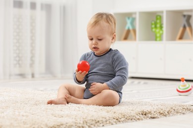 Children toys. Cute little boy playing with red ball on rug at home