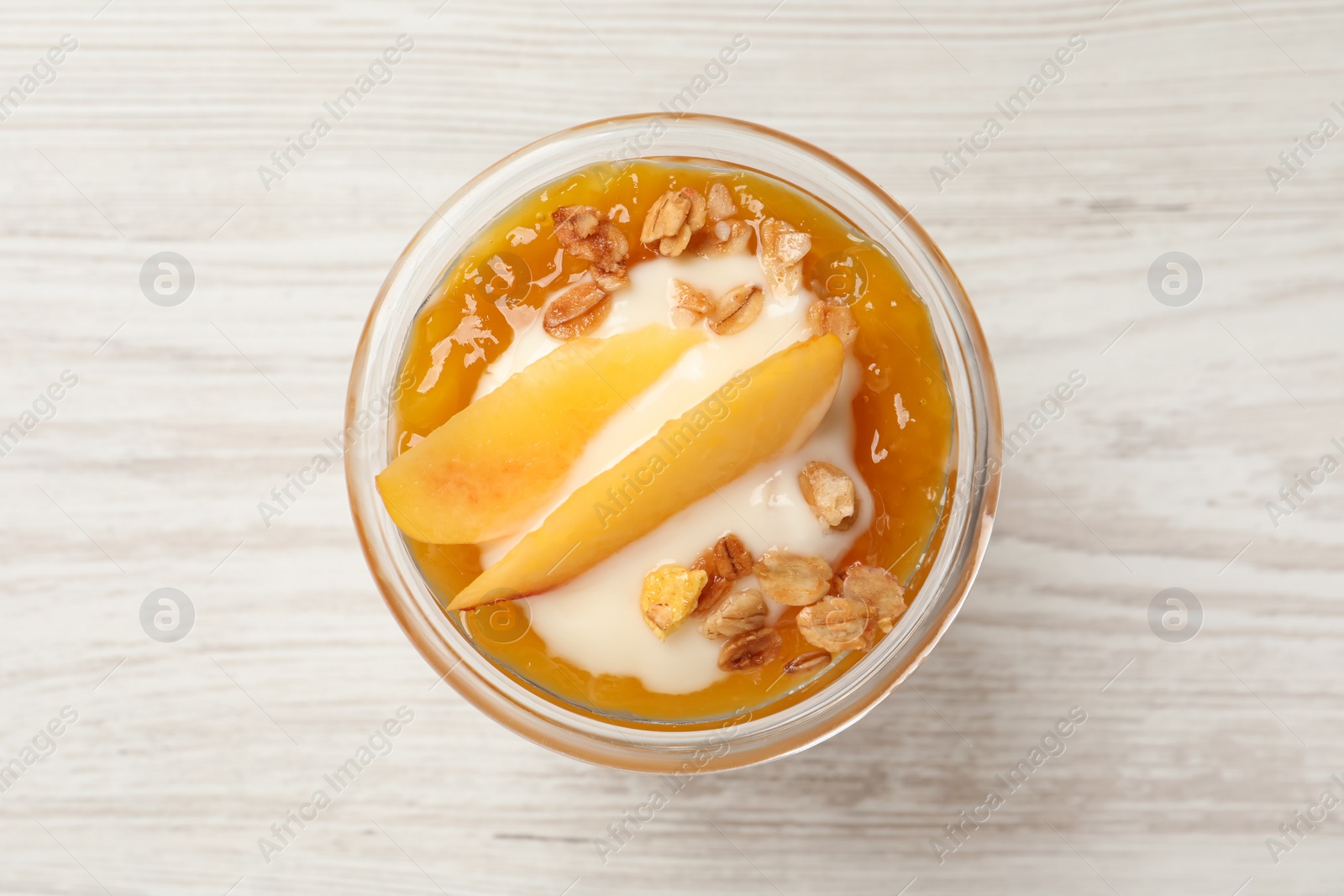 Photo of Tasty peach yogurt with granola, jam and pieces of fruit in glass on white wooden table, top view