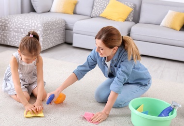 Housewife with daughter cleaning carpet in room together