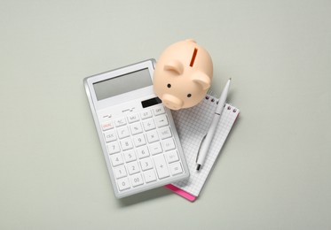 Photo of Calculator, piggy bank, notebook and pen on light grey background, flat lay