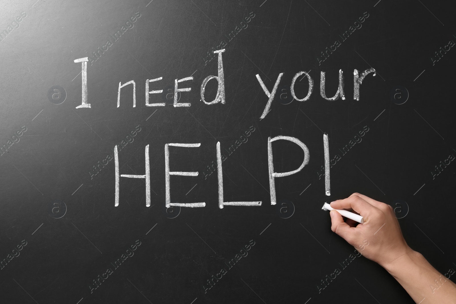 Photo of Man writing phrase "I need your help" on chalkboard, closeup