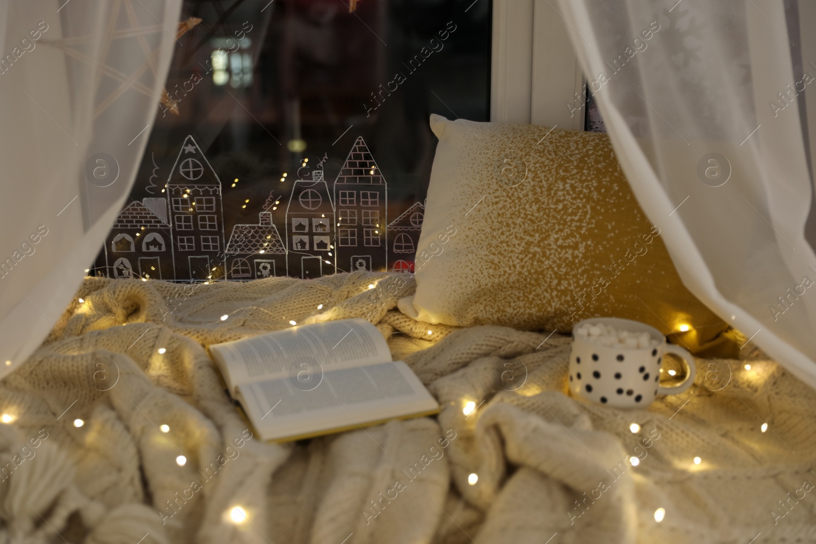 Photo of Open book and cup of hot drink on plaid near window with beautiful drawing at home. Christmas decor