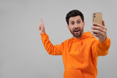 Photo of Emotional man taking selfie with smartphone on grey background, space for text