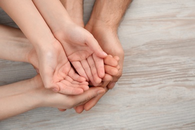 Photo of Top view of parents and kid holding empty hands together at wooden table, space for text. Family day