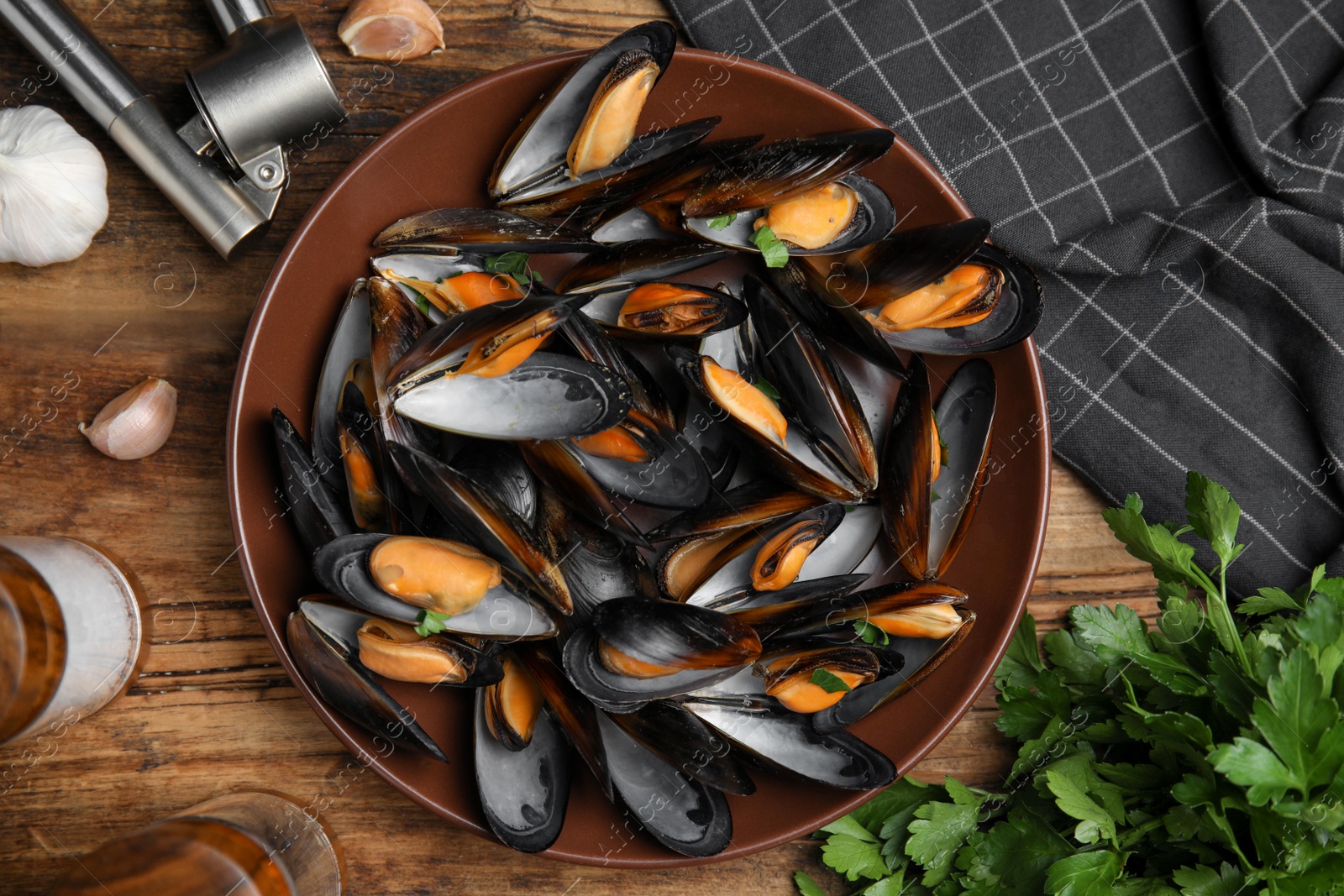 Photo of Plate of cooked mussels with parsley and garlic on wooden table, flat lay