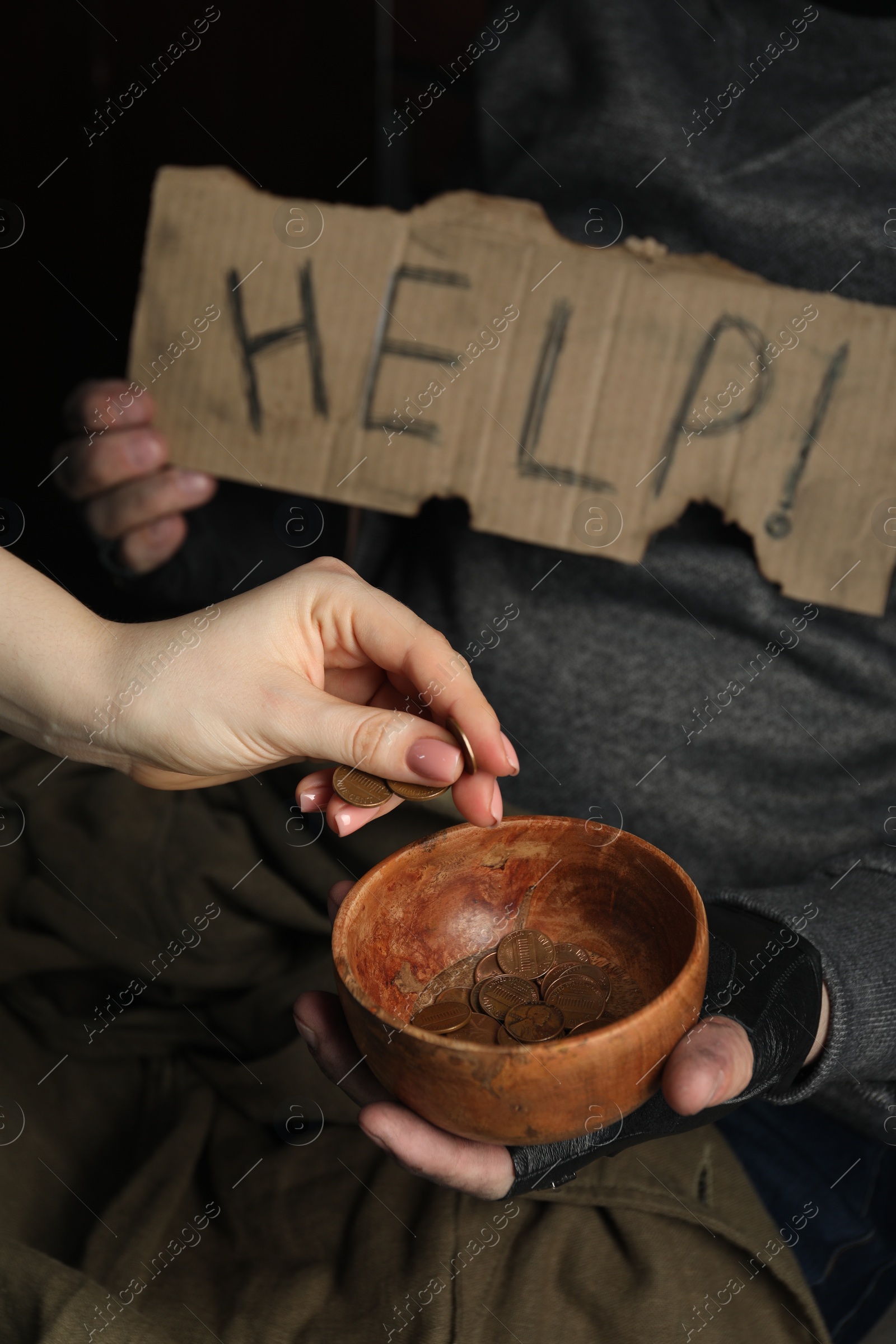 Photo of Woman giving coins to poor homeless man with bowl of donations and help sign on dark background, closeup