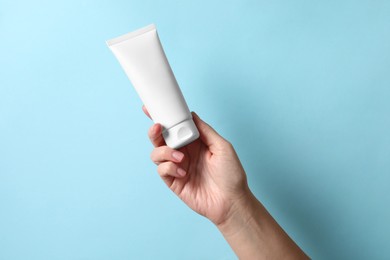 Photo of Woman with tube of hand cream on light blue background, closeup