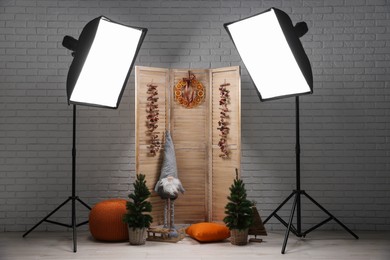 Photo of Beautiful Christmas themed photo zone with professional equipment and small trees near white brick wall