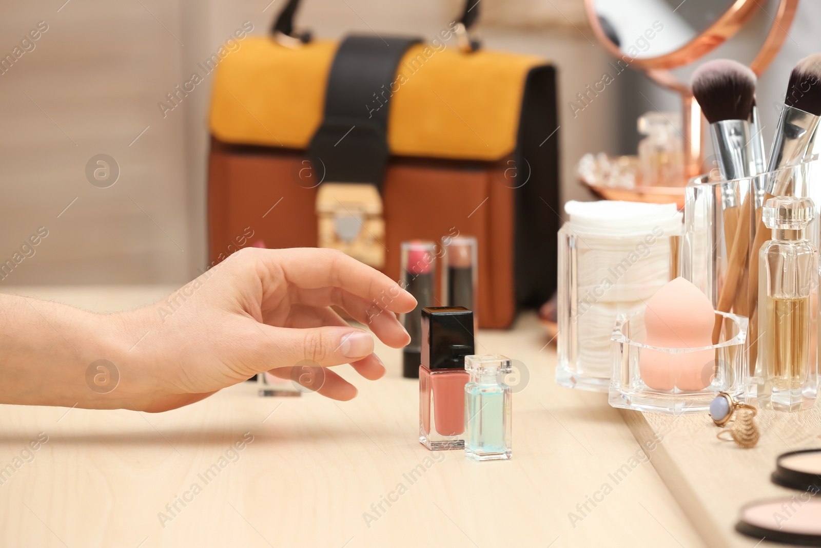 Photo of Woman reaching for cosmetic products on dressing table, closeup. Professional makeup