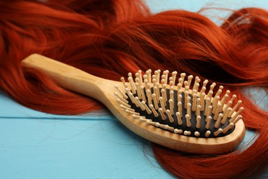 Brush and red hair strand on light blue wooden table