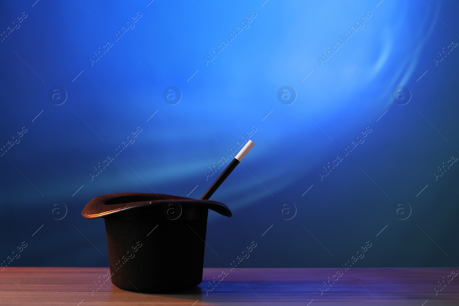 Photo of Magician's hat and wand on wooden table against blue background, space for text